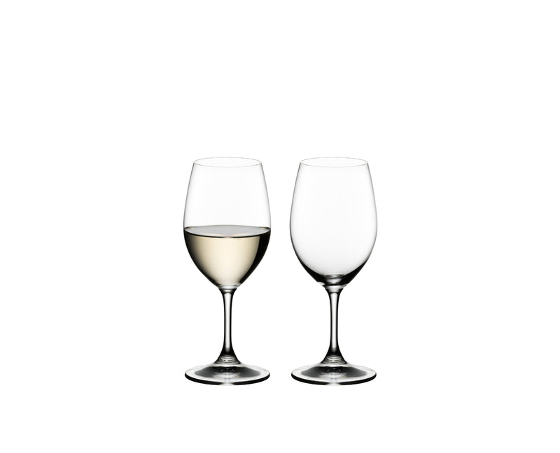 Two Riedel Ouverture white wine glasses, one filled with white wine and one empty, on a white background